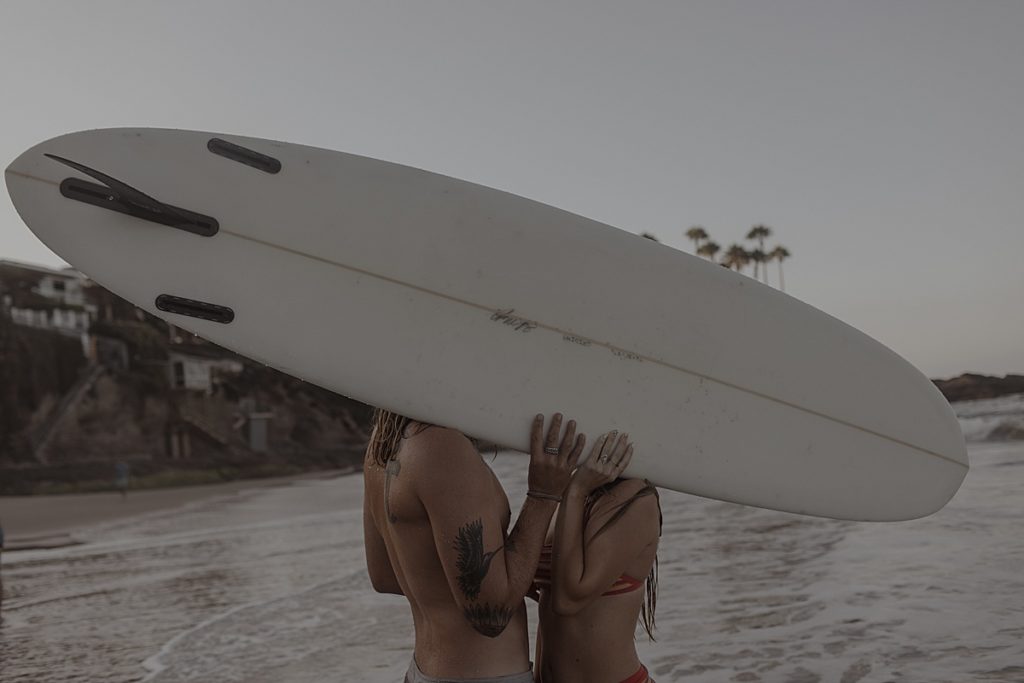 couple on beach holding surfboard