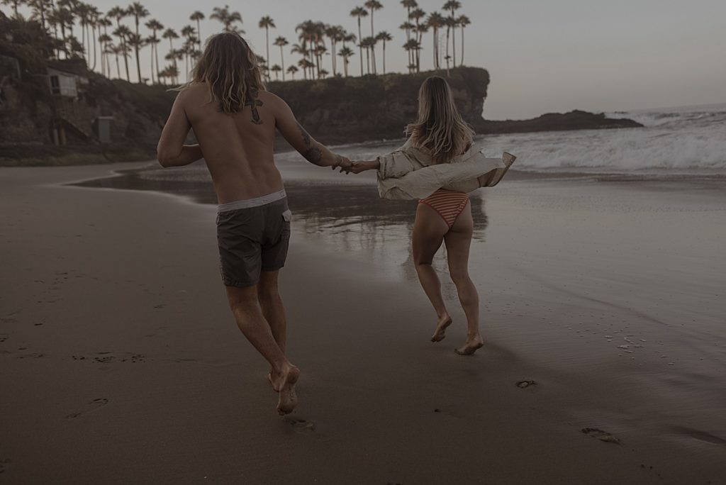 couple running on beach holding hands in laguna