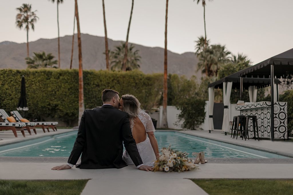 bride and groom sitting at pool during their wedding day