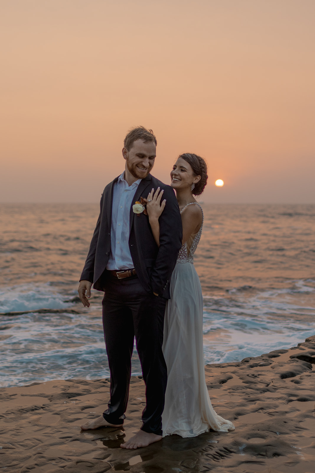 bride and groom standing on cliffside during beach elopement in san diego at sunset