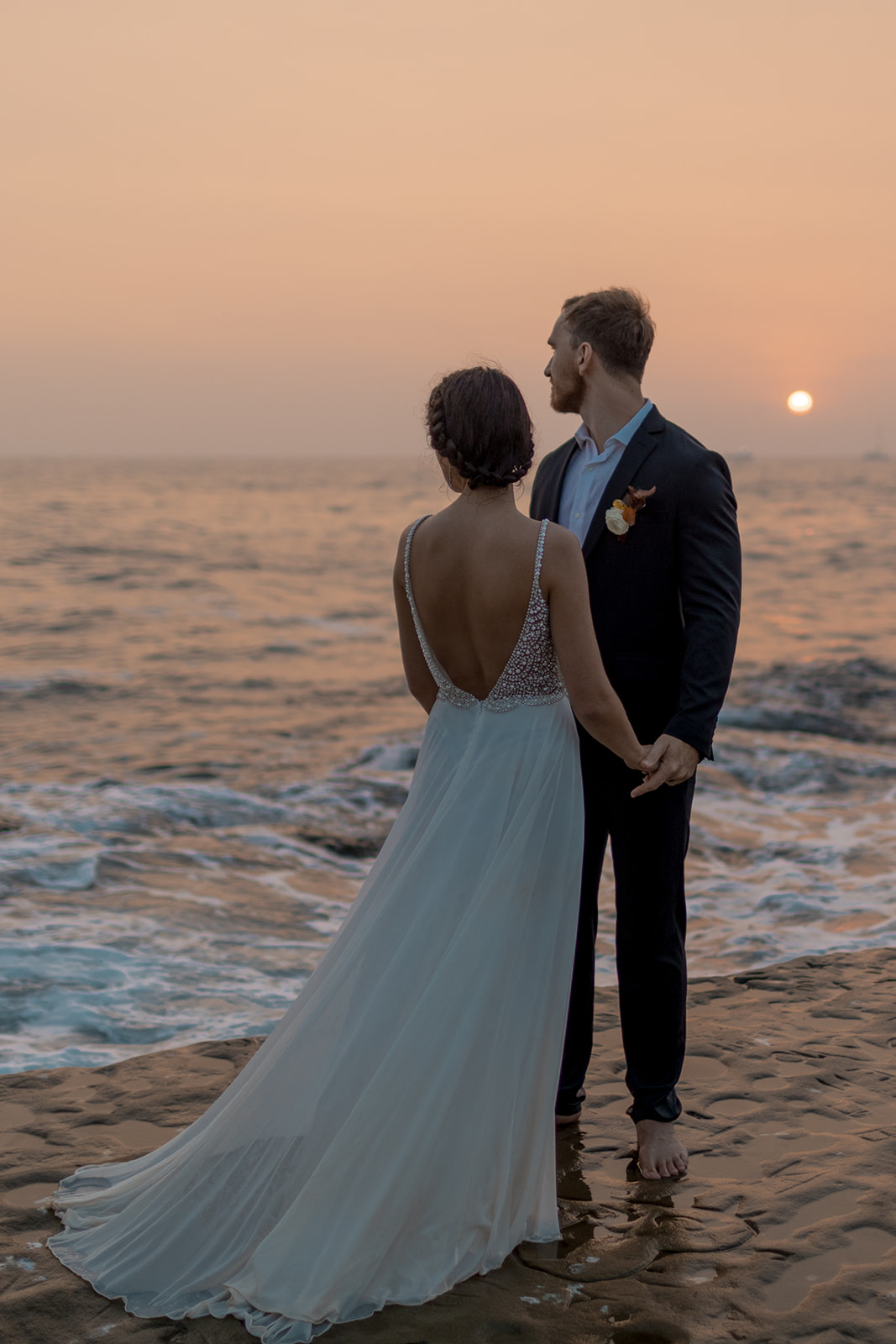 bride and groom standing on cliffside during beach elopement in san diego at sunset
