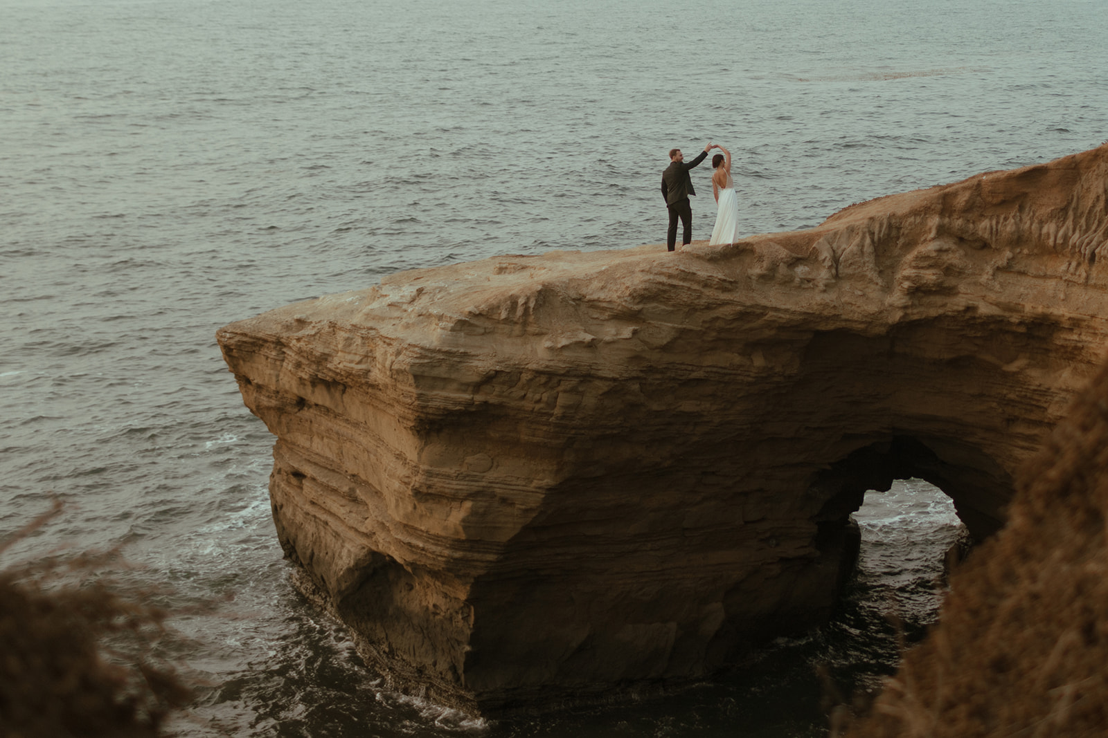 bride and groom dancing on cliff side in san diego with beautiful beach backdrop