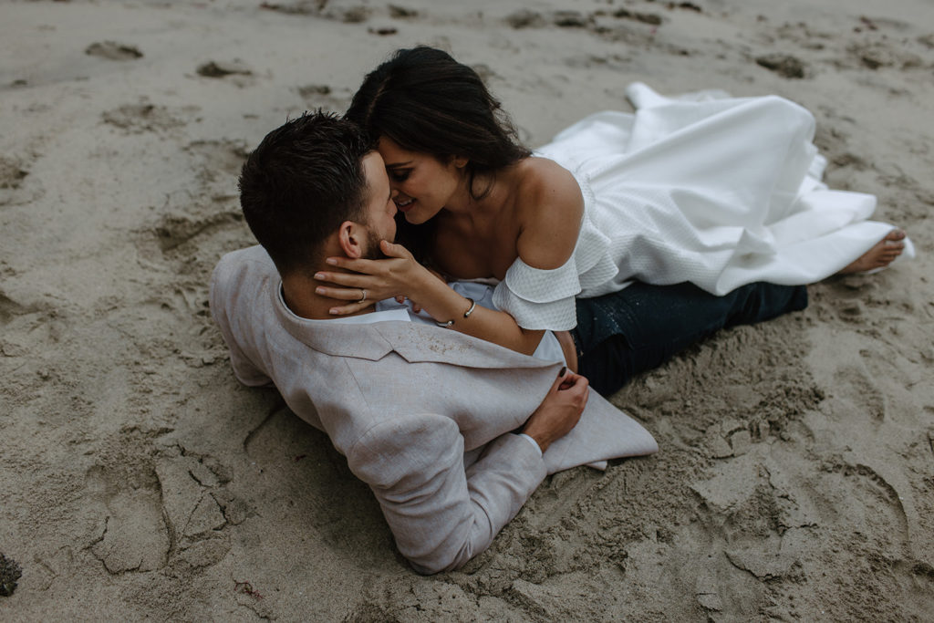 bride and groom laying on sand at beach elopement
