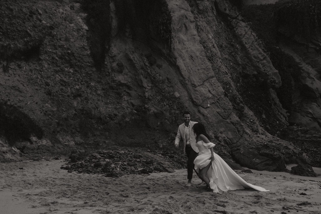 couple running through sand at beach wedding