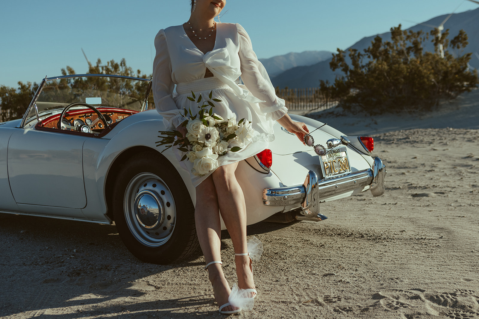 Retro Palm Springs Elopement with bride wearing short dress and holding white florals
